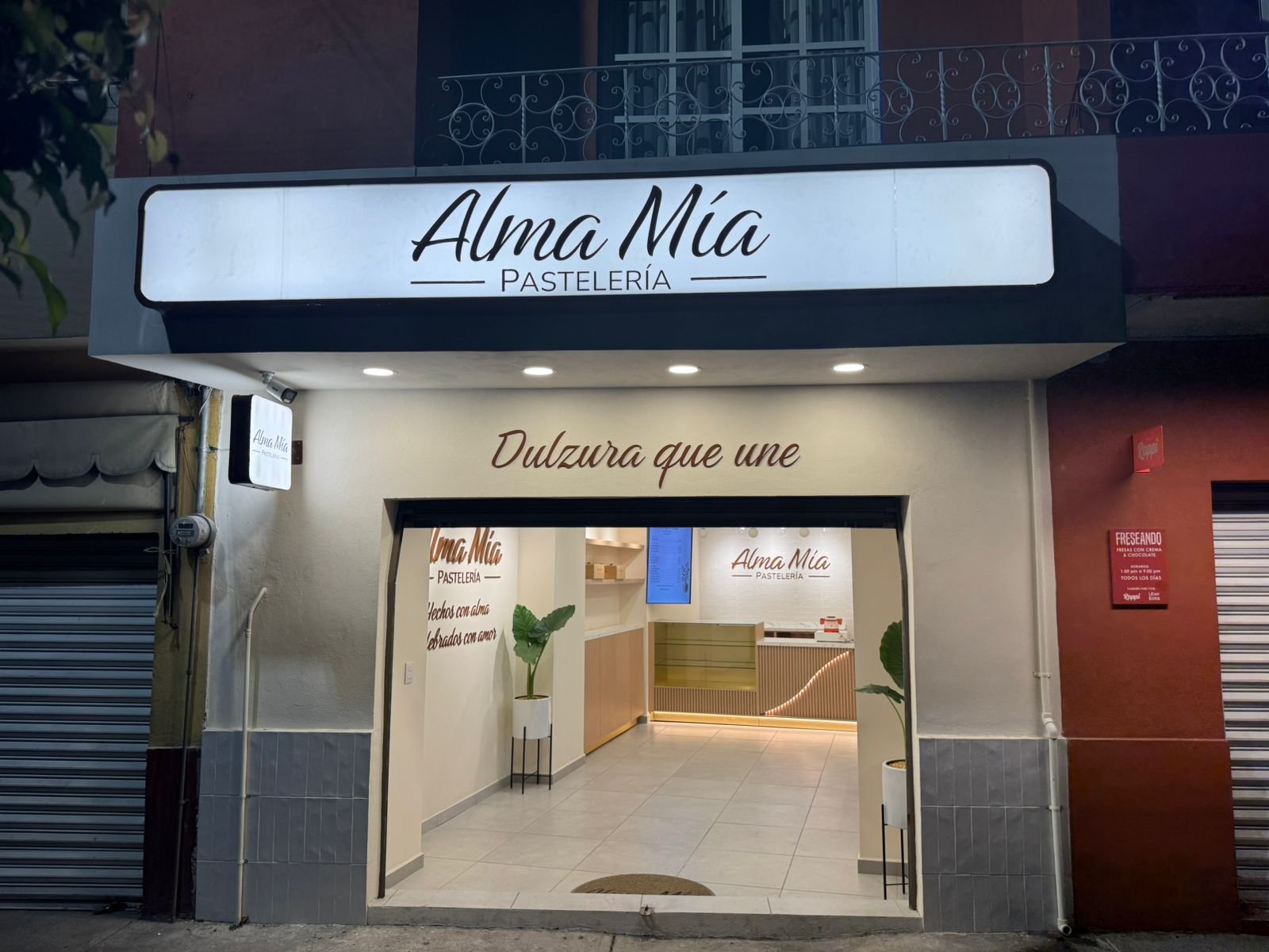 Alma Mia pastelería storefront with illuminated window display and dulzura que une tagline on glass door