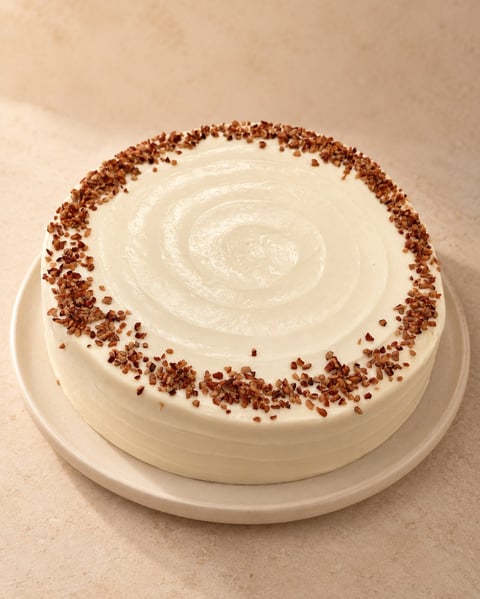Round white frosted cake with chocolate cake crumbs border and spiral decoration on top, displayed on a white cake plate